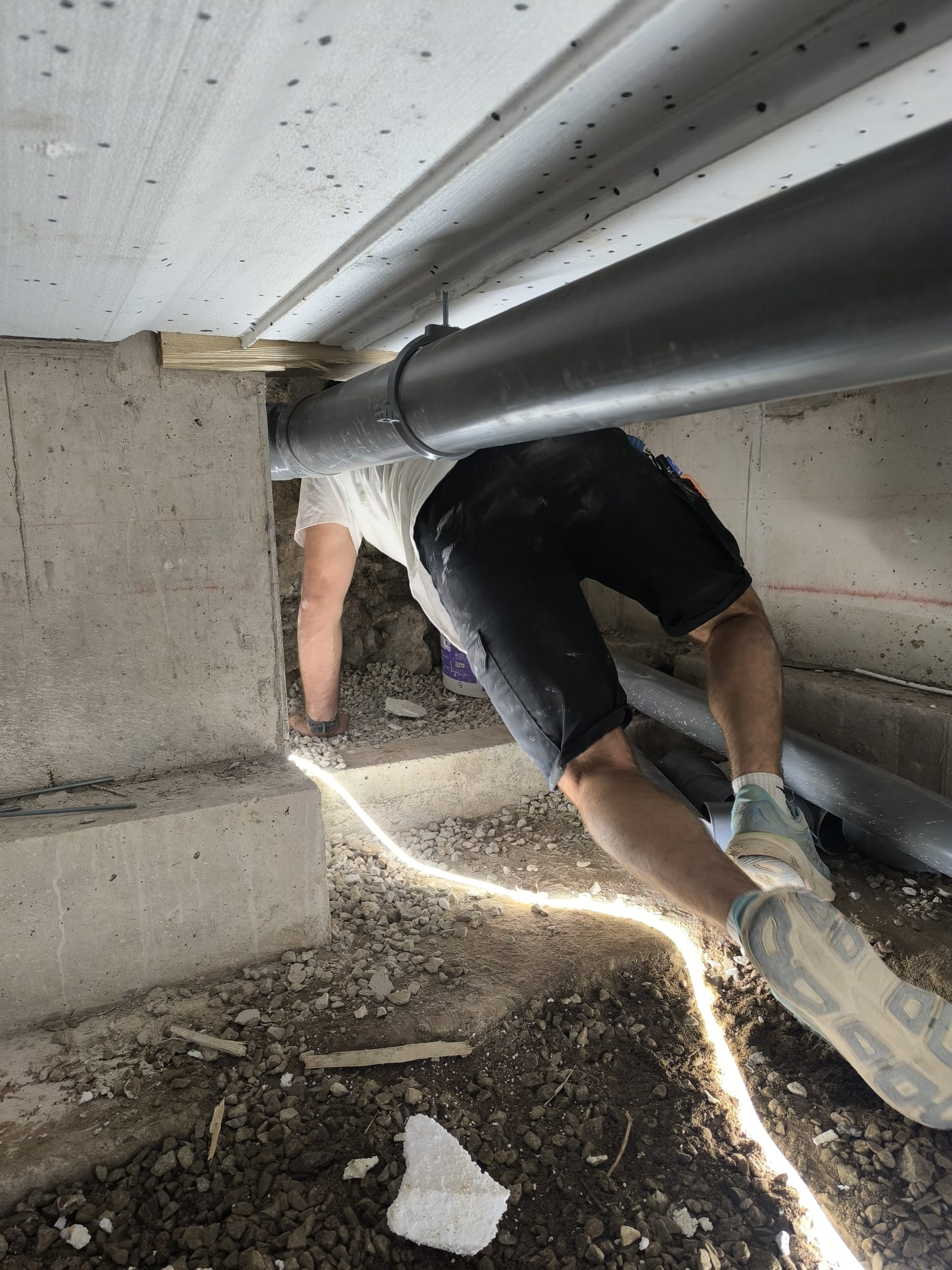 Artisan travaillant sur des canalisations sous un plancher, dans un espace de faible hauteur